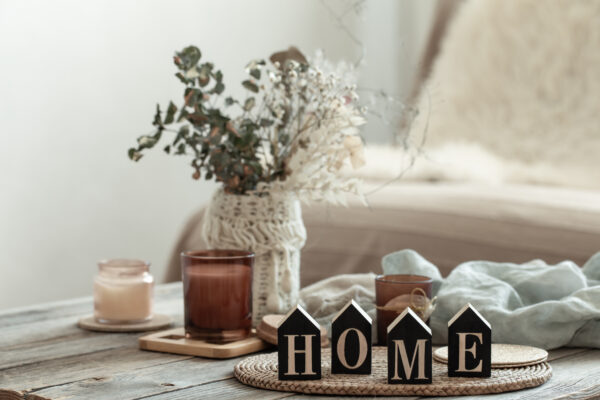 Close up decorative word home on blurred background with candles. Cozy home background with decorative word home, bouquet and candles on blurry background.